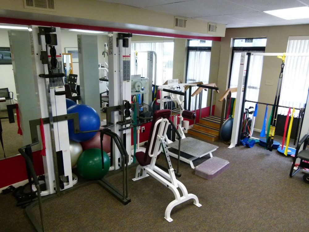 A physical therapy or rehabilitation gym featuring exercise machines, balance balls, and training equipment.