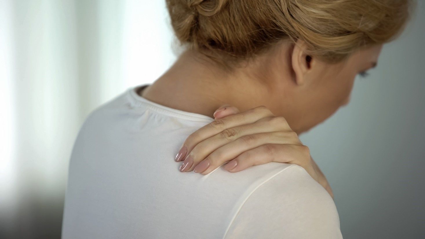 Woman holding her shoulder, appearing in pain.