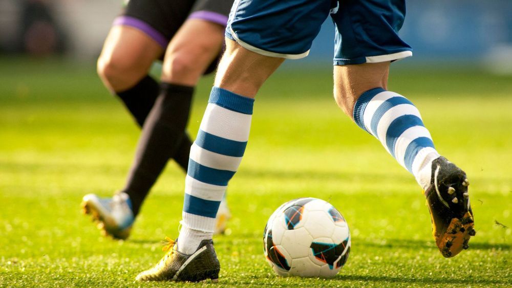 Two soccer players competing for the ball on a grassy field, focusing on their legs and feet in motion.