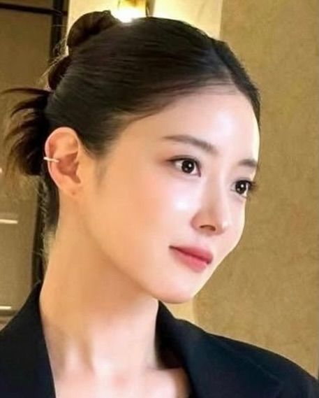 Woman with dark hair in a bun, wearing a black top and ear cuff, looking to the side.