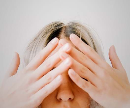 Person covering eyes with hands; neutral expression.