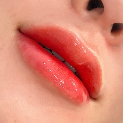 Close-up of glossy, red lips, slightly parted, on fair skin.
