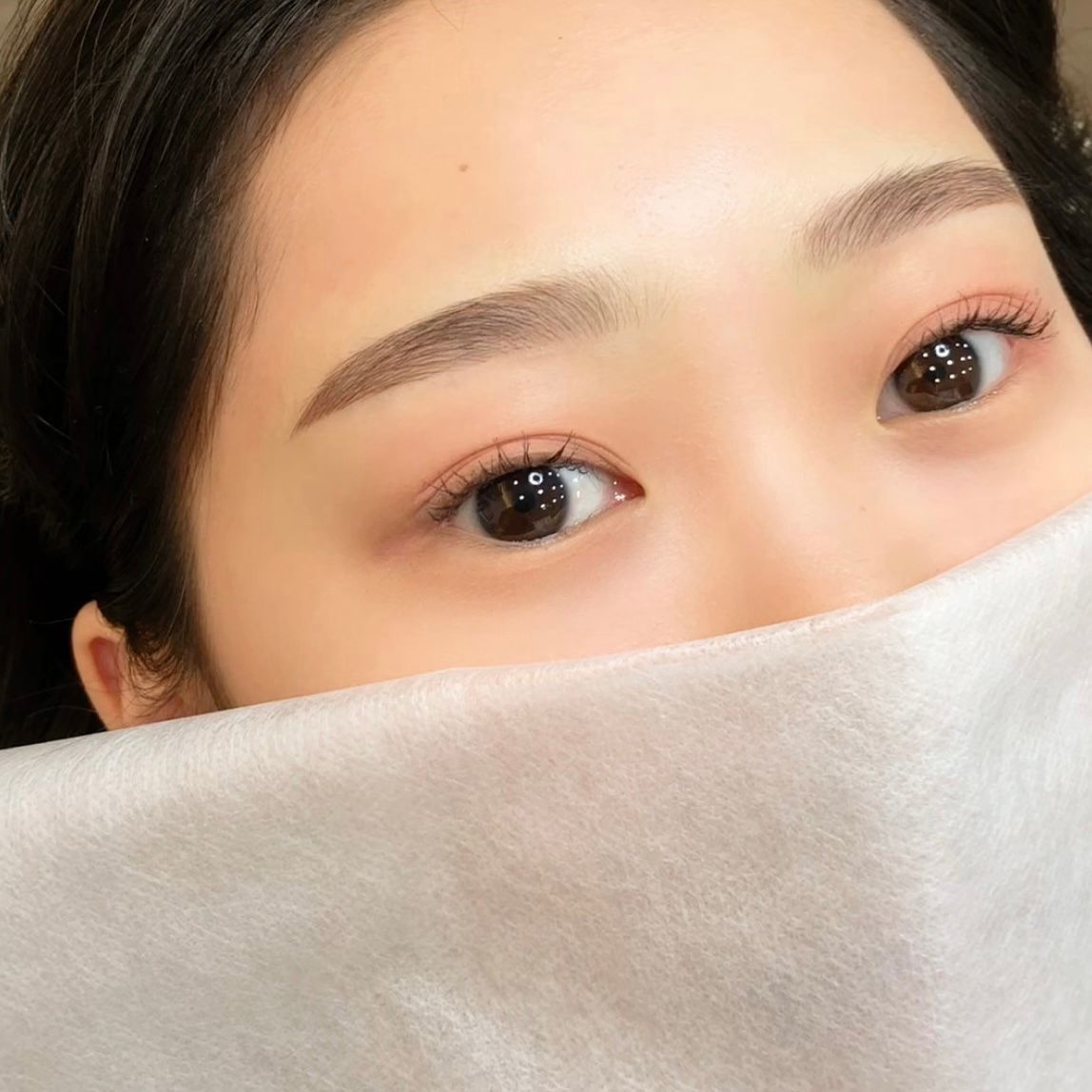 Close-up of a face with expressive eyes, partly covered by a soft light-gray fabric mask