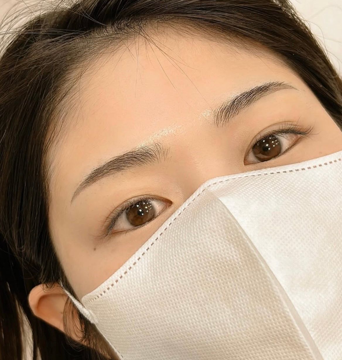 Close-up of a person wearing a white face mask, with only their eyes and forehead visible.