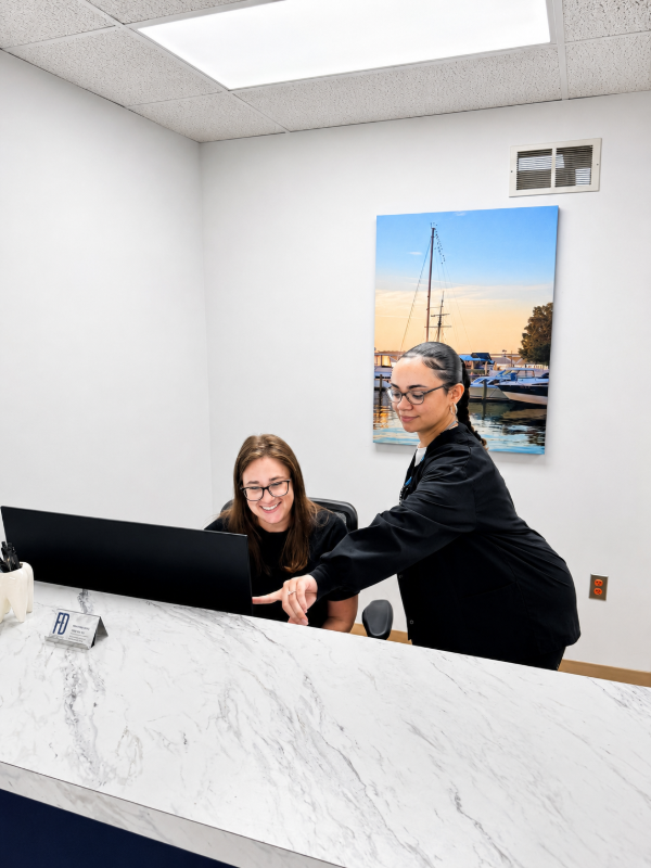 Two people at a reception desk in a bright office, smiling and working together.