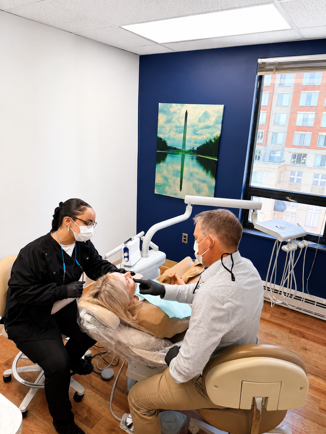 Dental exam with clinician and patient in a bright treatment room, blue accent wall and window in background