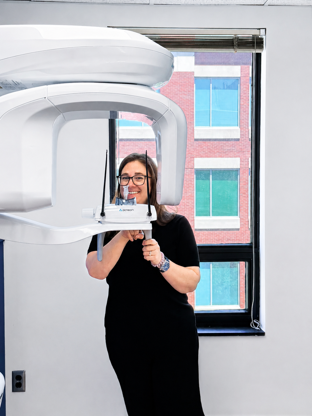 Person standing beside a large medical imaging machine, holding a control panel in a clinic room.