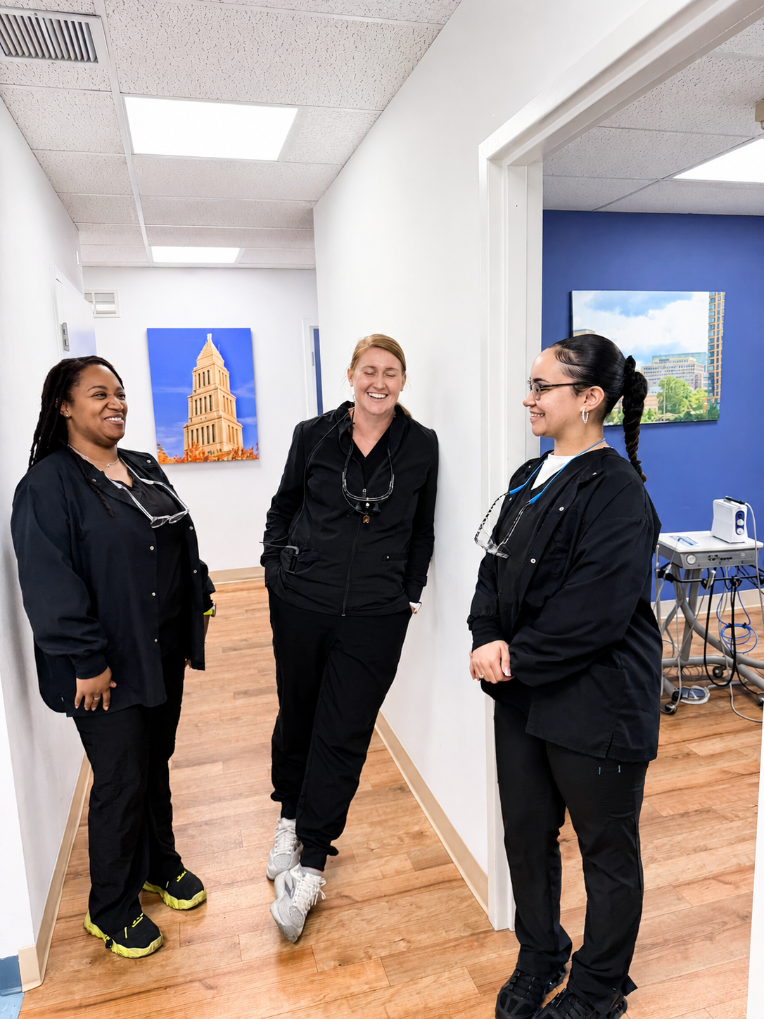 Three people in black outfits standing in a hallway with framed artwork and a drum set visible.