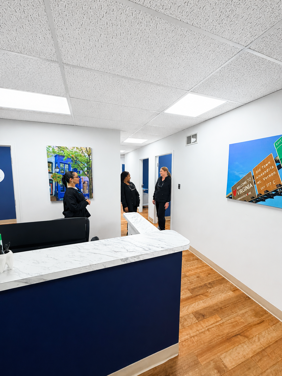 Bright office lobby with three people near blue walls, white ceiling lights, and wood flooring.
