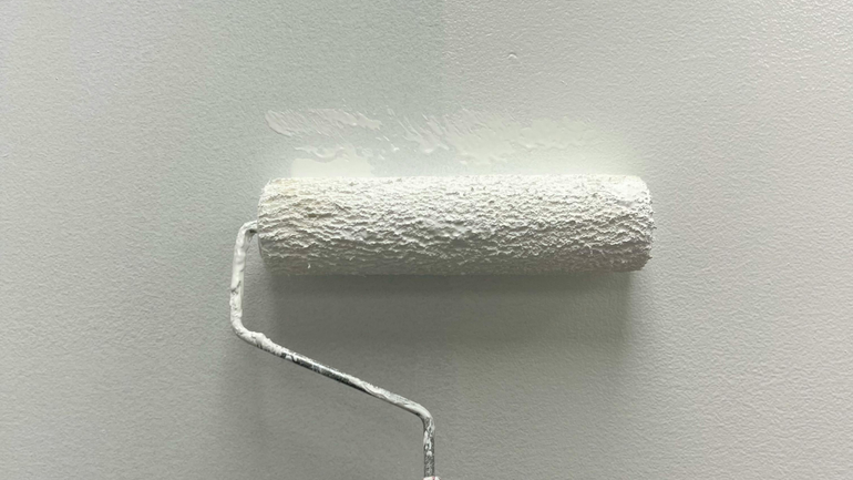 White paint roller on a white wall, applying a fresh coat.