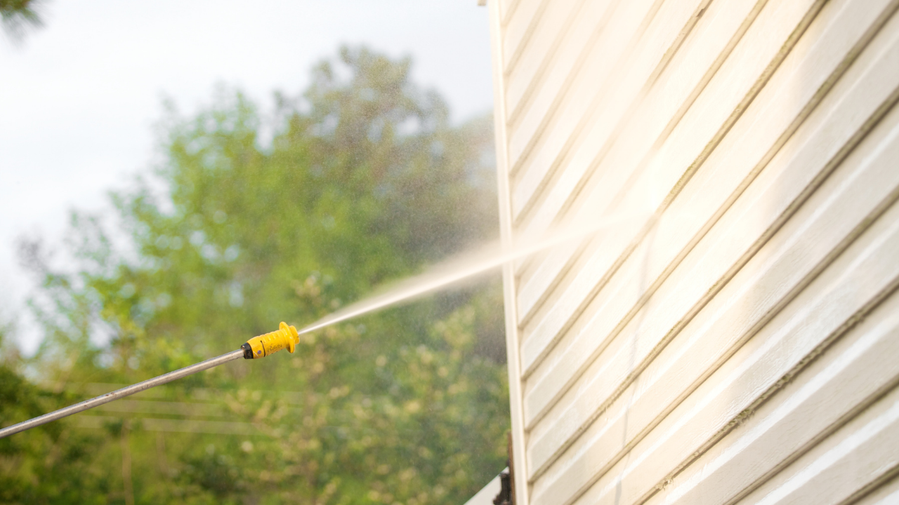Pressure washing a white vinyl siding house exterior.