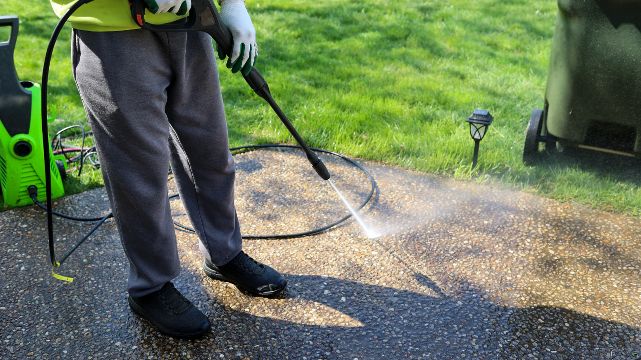 Person pressure washing a concrete surface with water, outdoors.