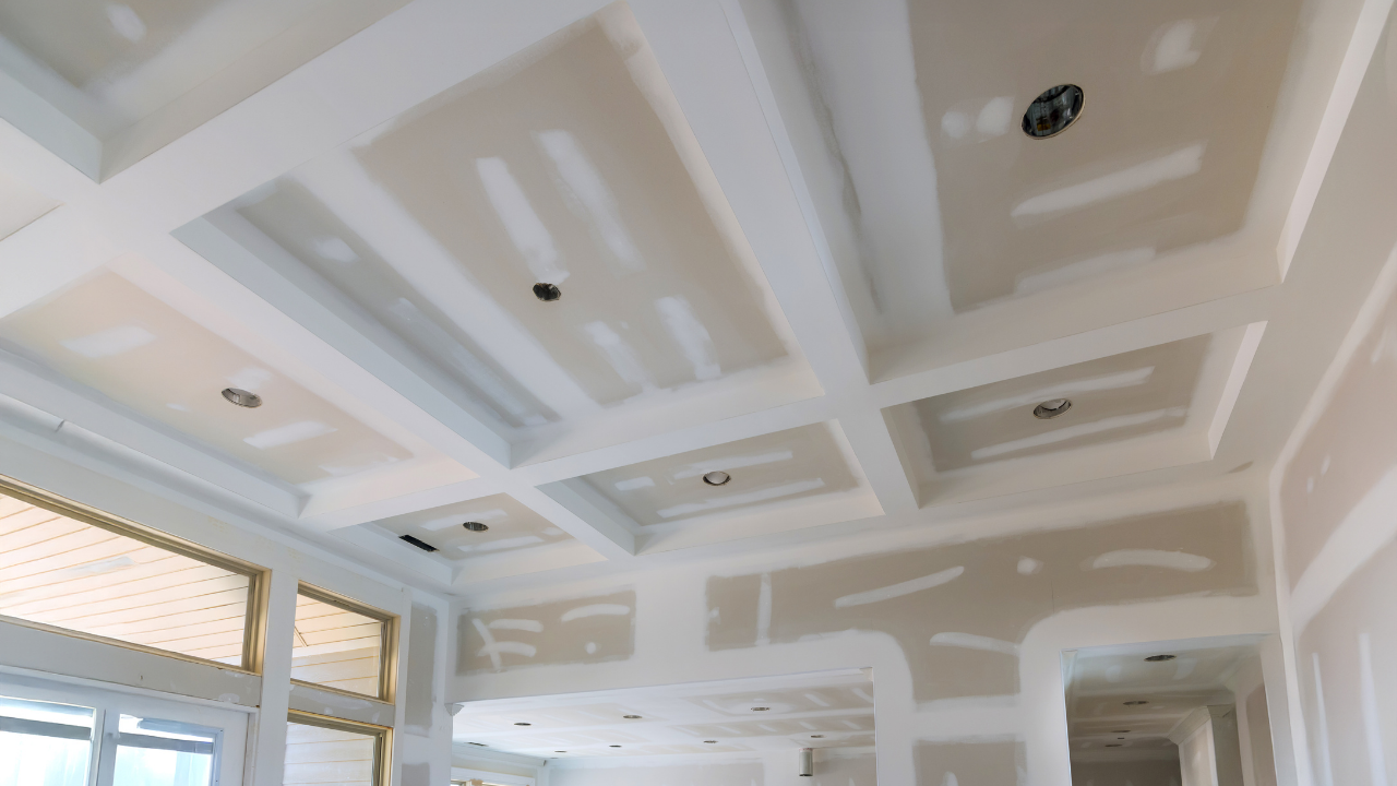 Drywall ceiling with recessed lighting and beams in a partially constructed room.