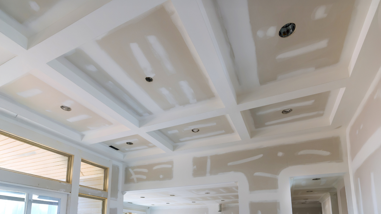 Drywall ceiling under construction with recessed lighting and beams.