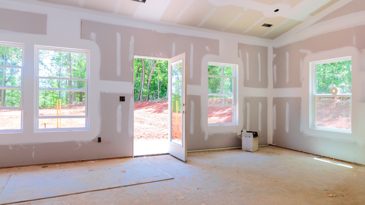 Interior of a room under construction, with drywall walls, windows, and an open doorway.