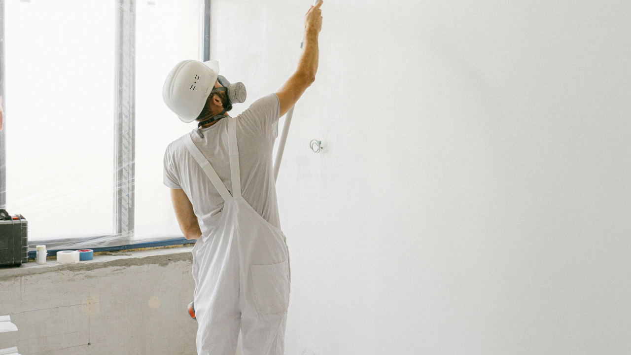 Person in white protective gear sprays paint on a white wall.