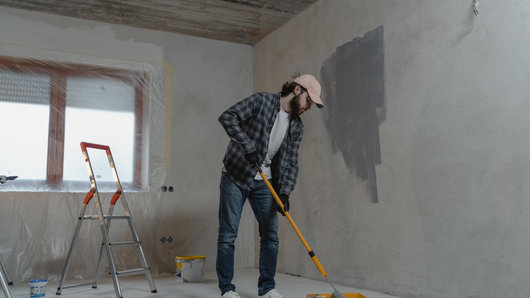 Man painting a wall gray with a roller in a room under renovation.