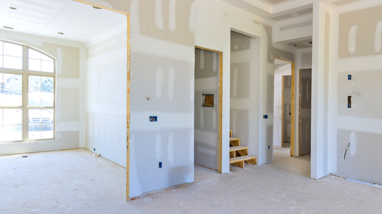 Interior of a house under construction; drywall covers walls and ceiling, with unfinished doorways and a window.