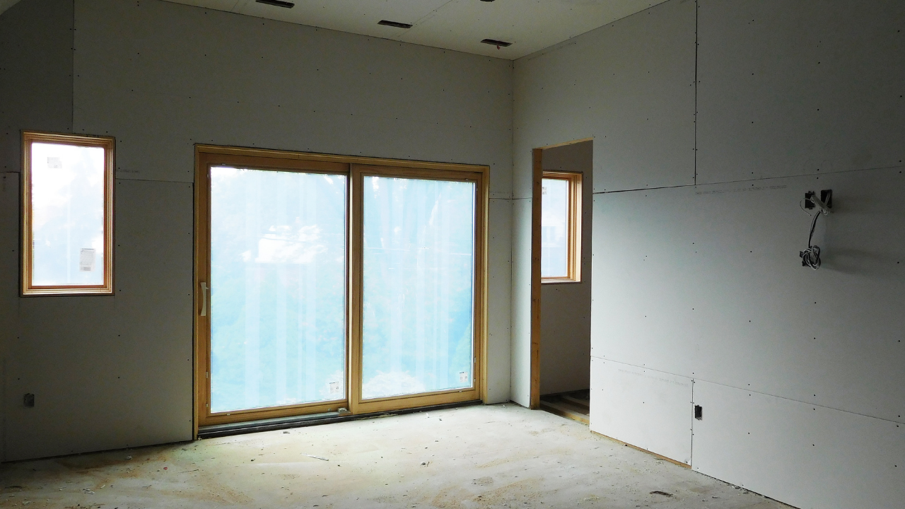 Interior of a room under construction with sliding glass doors, a window, and unfinished drywall.