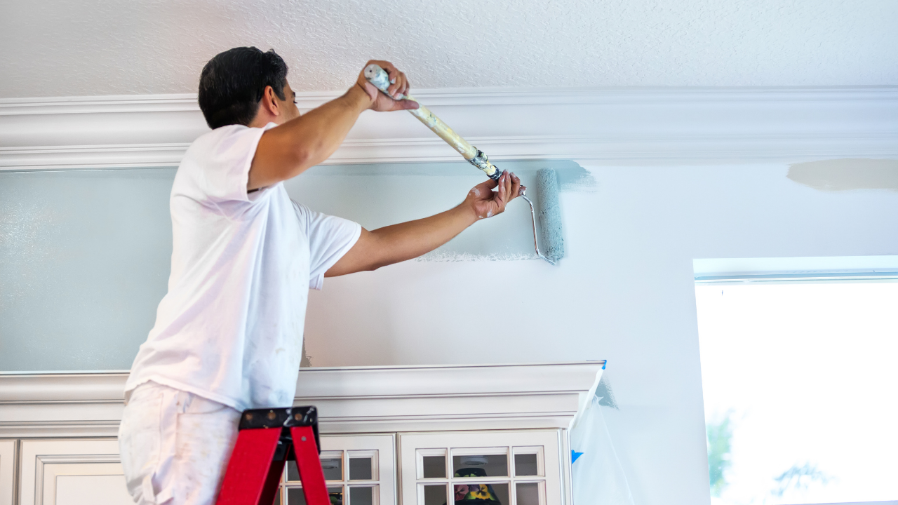 Person painting a wall blue from a step ladder indoors.
