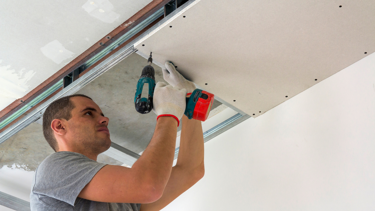 Person installs drywall on a ceiling using a power drill.