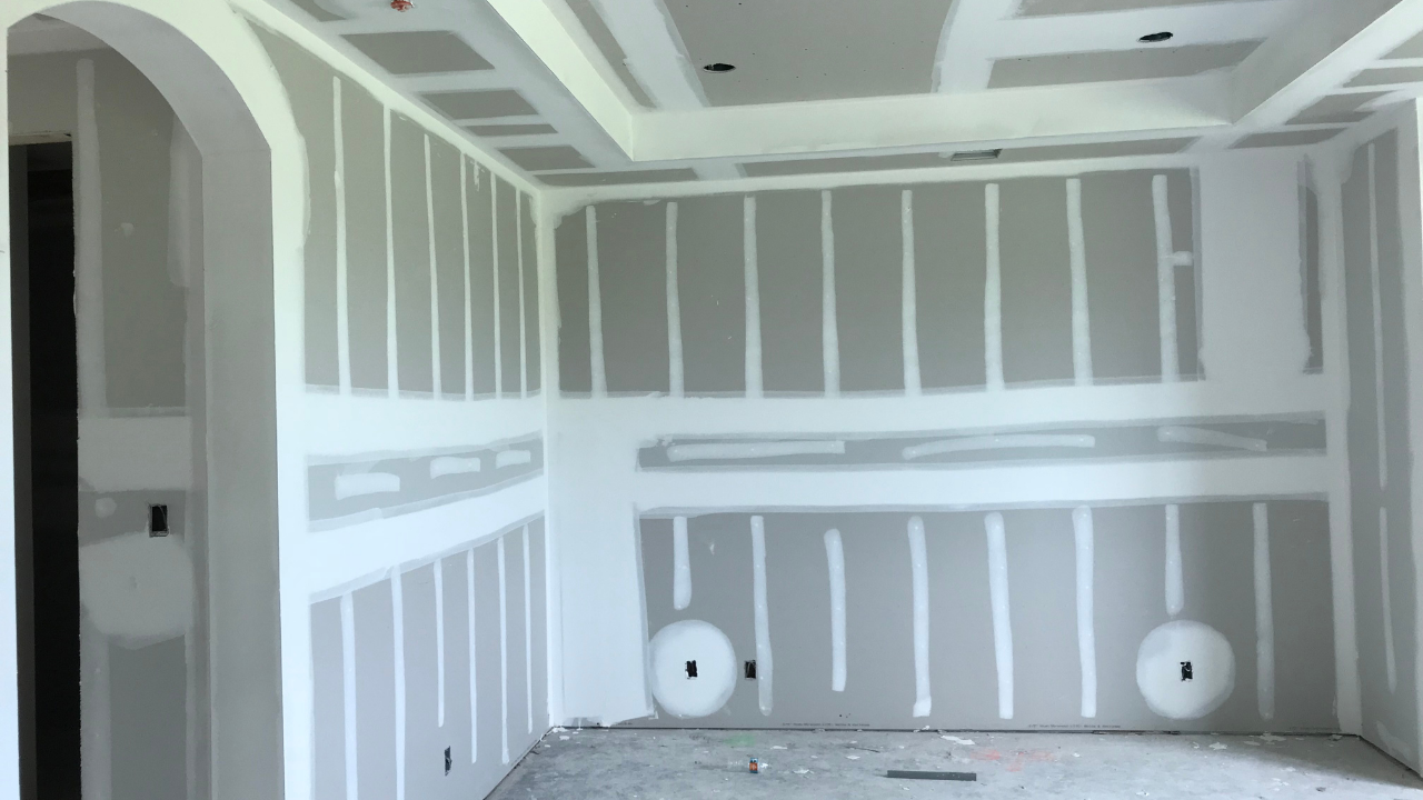 Interior room with drywall installation; walls and ceiling with white painted seams and an arched doorway.