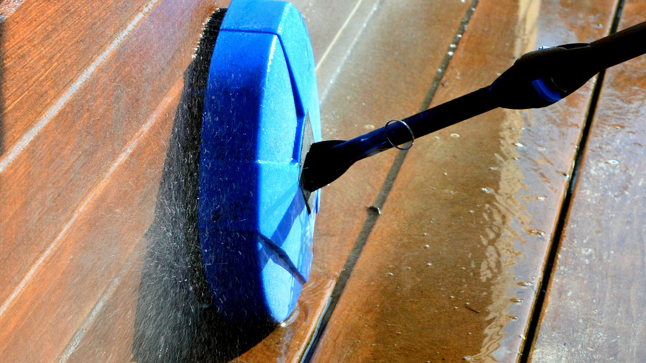 A pressure washer with blue scrubbing head cleaning a wooden deck.