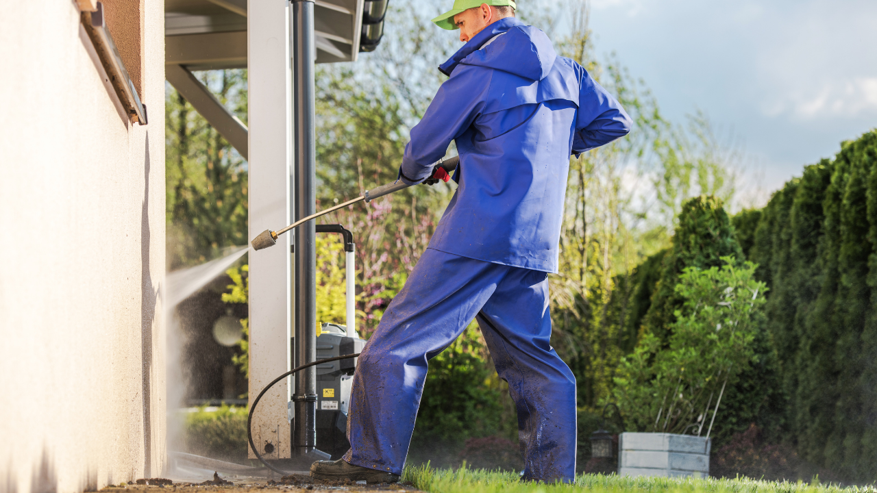 Person in blue coveralls power washing a building's exterior.