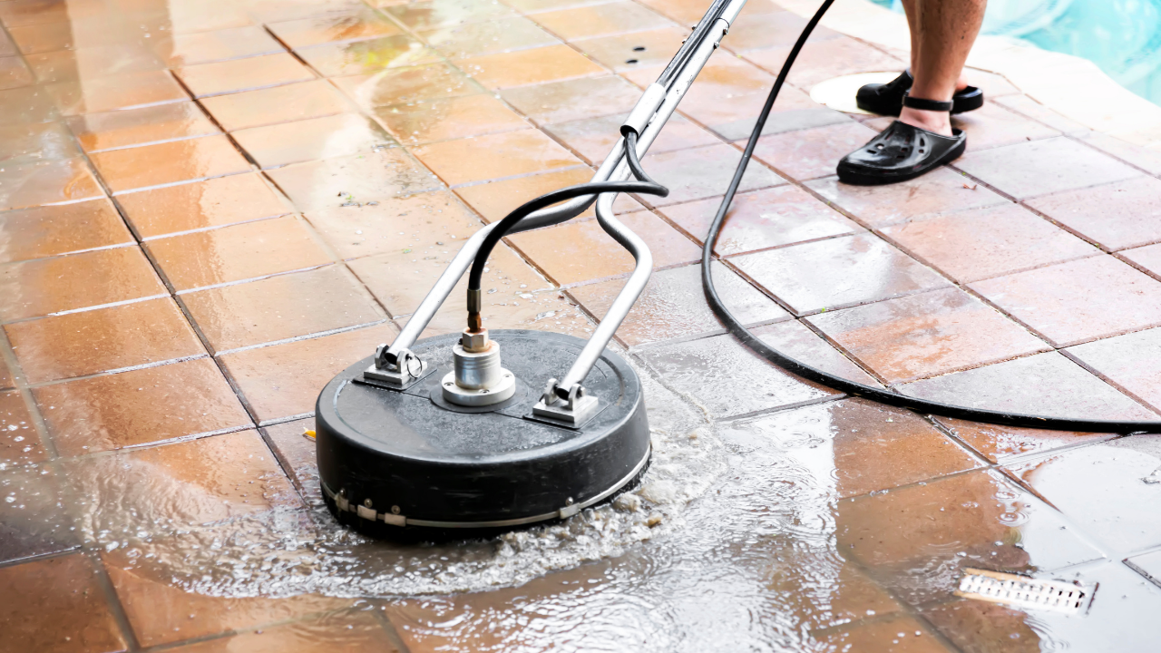 Person power washing a brick patio with a circular surface cleaner.