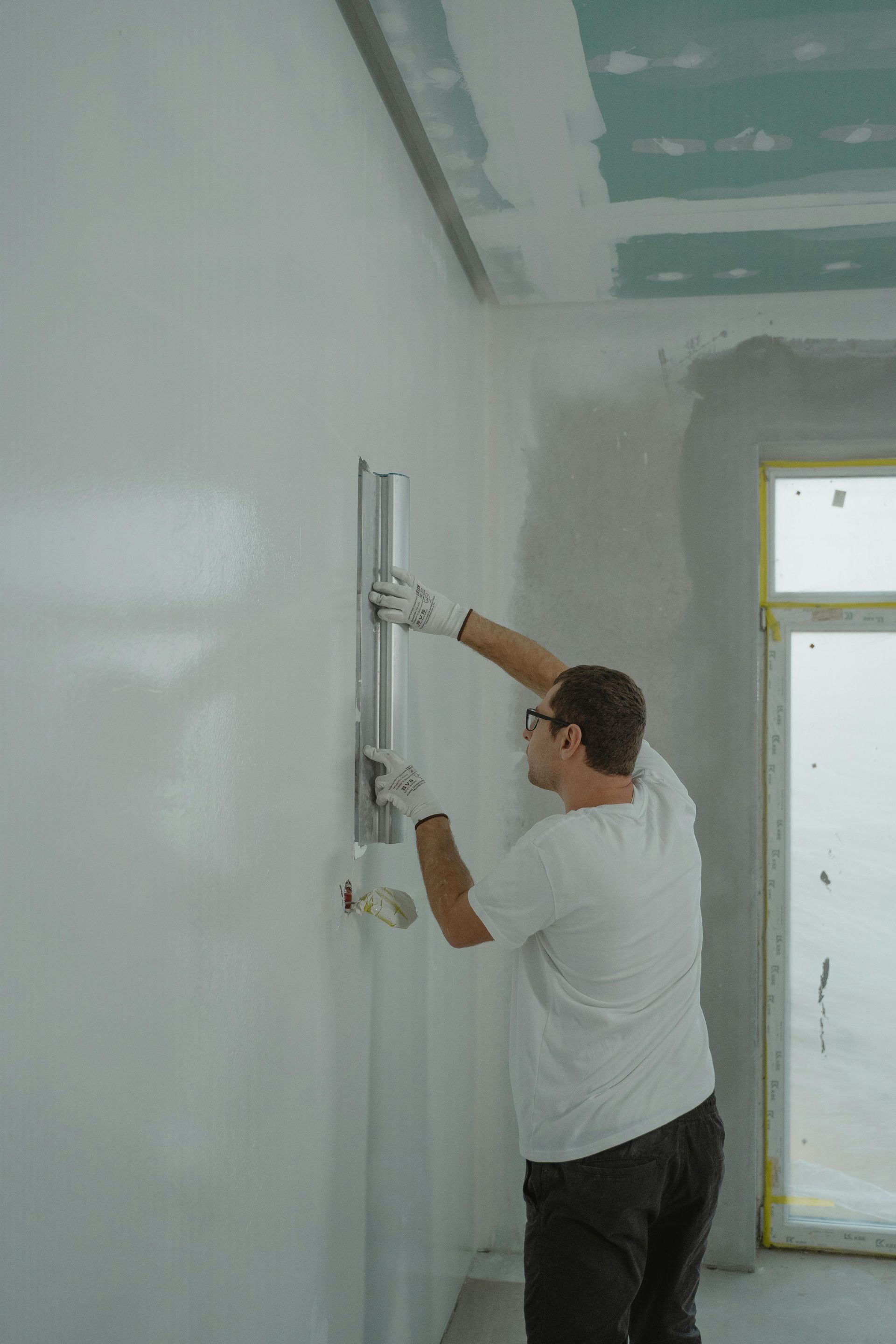 Man smoothing wall with a long trowel. White room, working on a construction project.