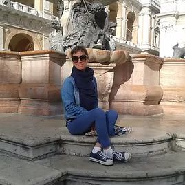 Person in blue sitting on a fountain ledge in front of an ornate stone sculpture.