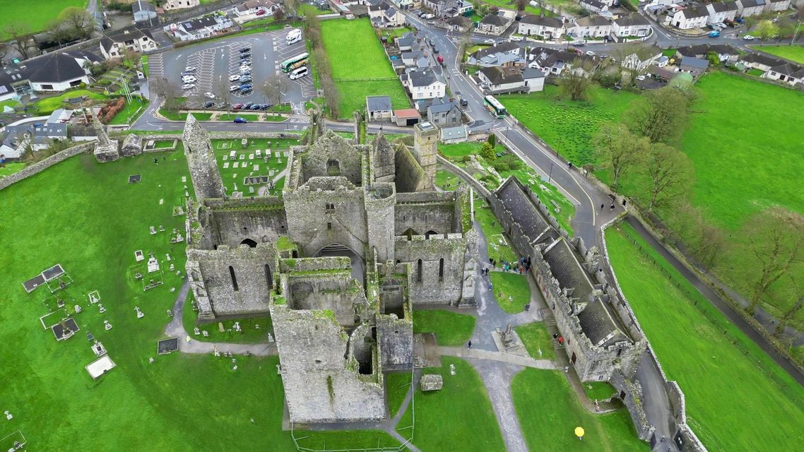 Aerial view of a large stone castle ruin surrounded by green fields and nearby houses.