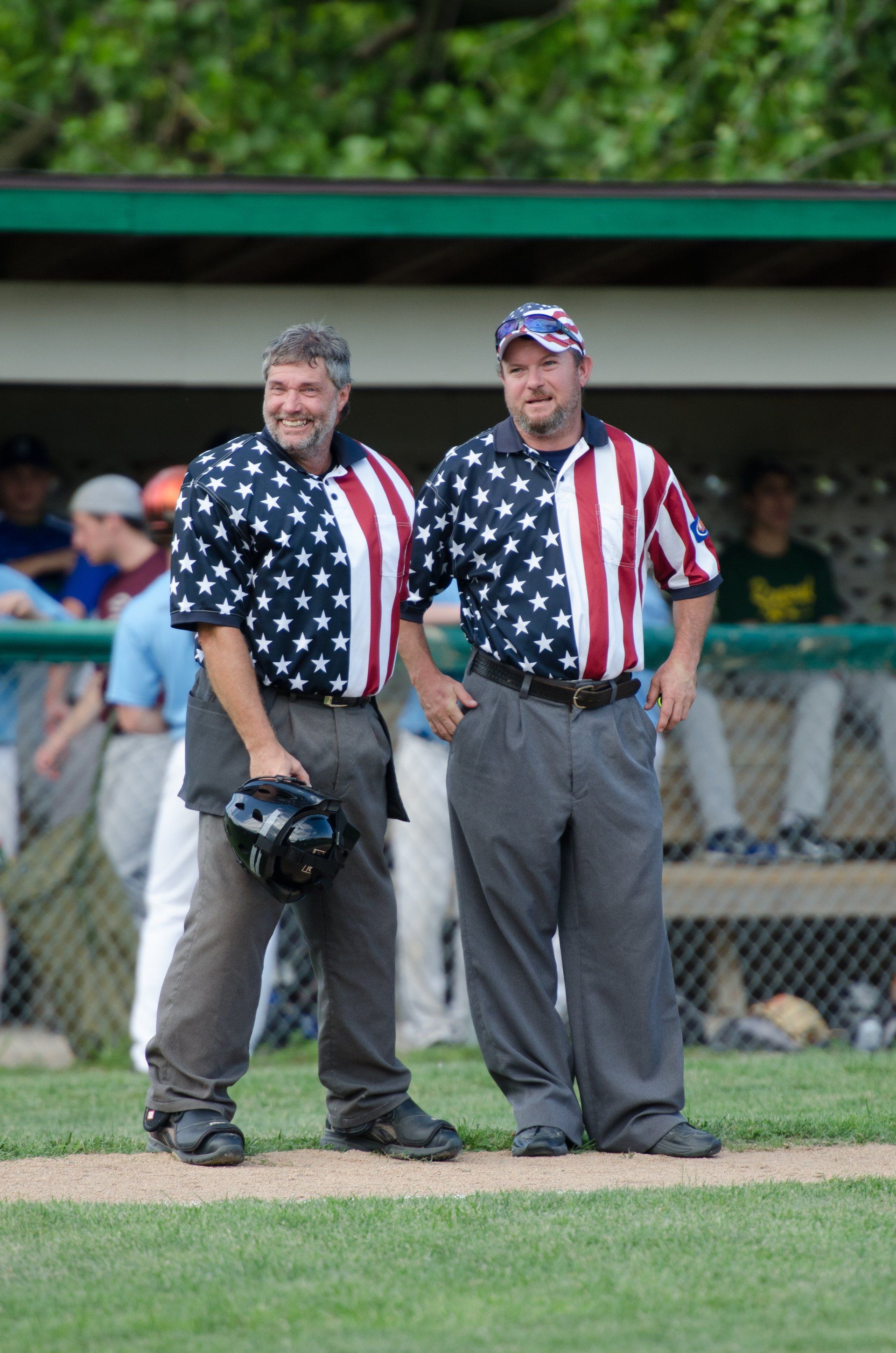 Two men in baseball umpire shirts stand on a baseball field.