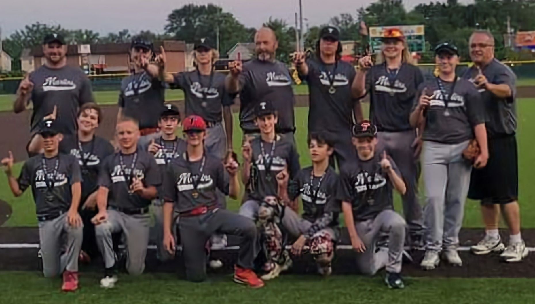 Baseball team in grey uniforms posing on a field, holding up 