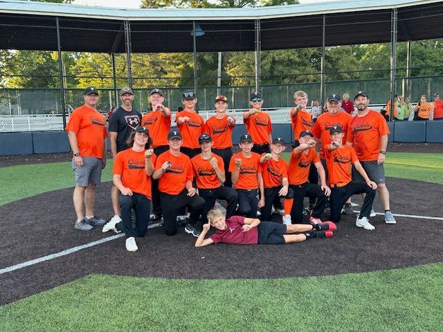 Baseball team in orange shirts poses on field; group photo.