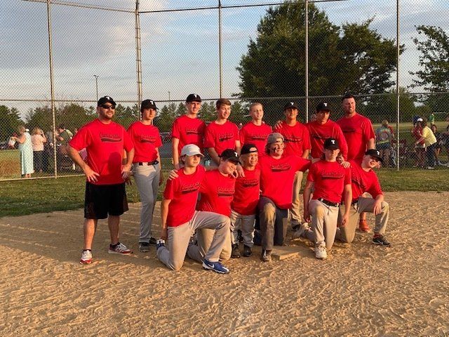 Baseball team in red shirts and hats, posing on a baseball field.