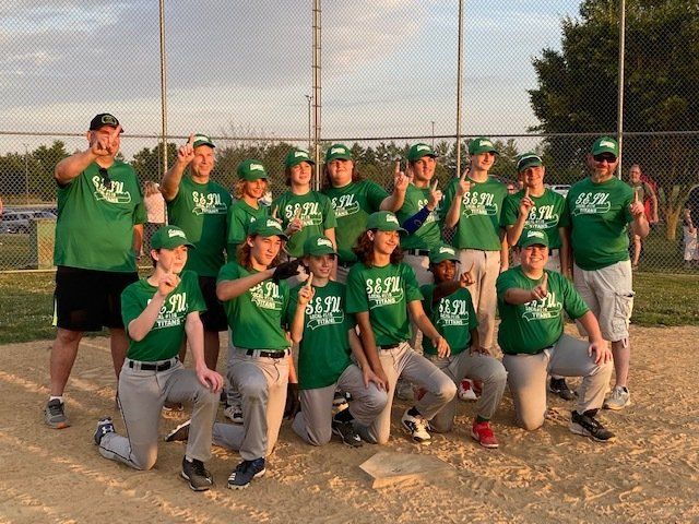 Youth baseball team in green uniforms, posing on the field, making hand gestures.
