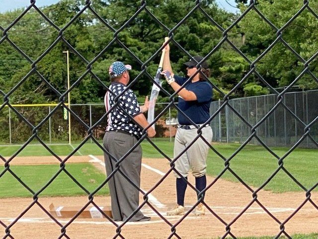 A softball player high-fives an umpire at home plate, behind a chain-link fence.