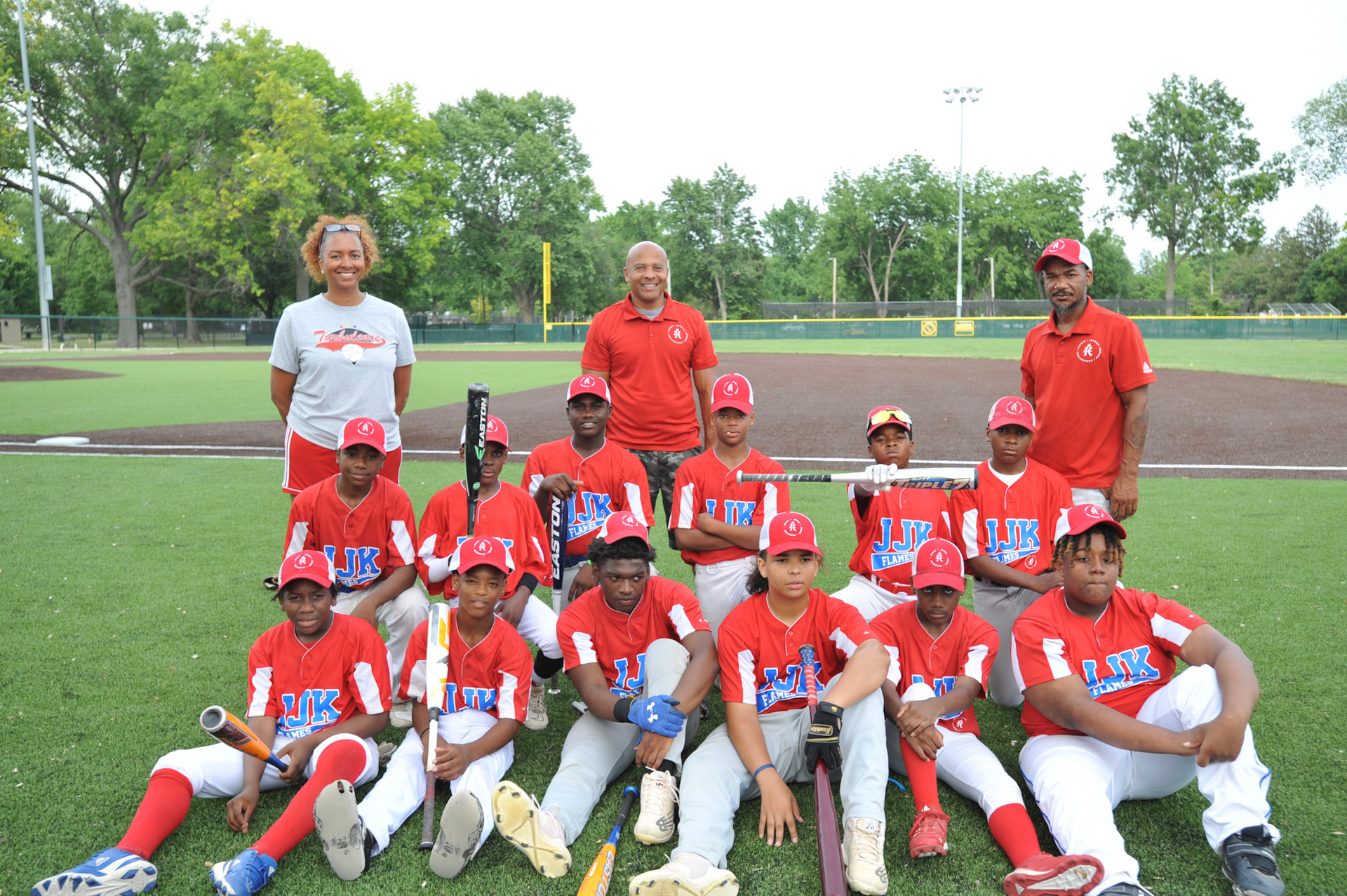 Baseball team in red uniforms, posed on a baseball field with coaches.