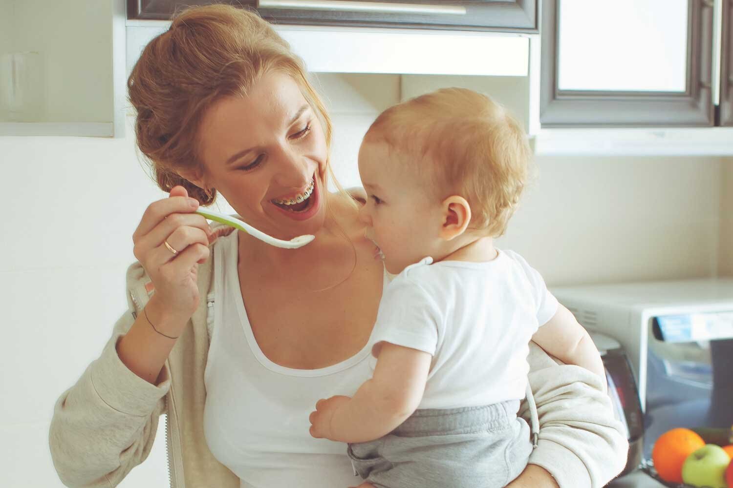 Smiling woman with braces feeding her baby.