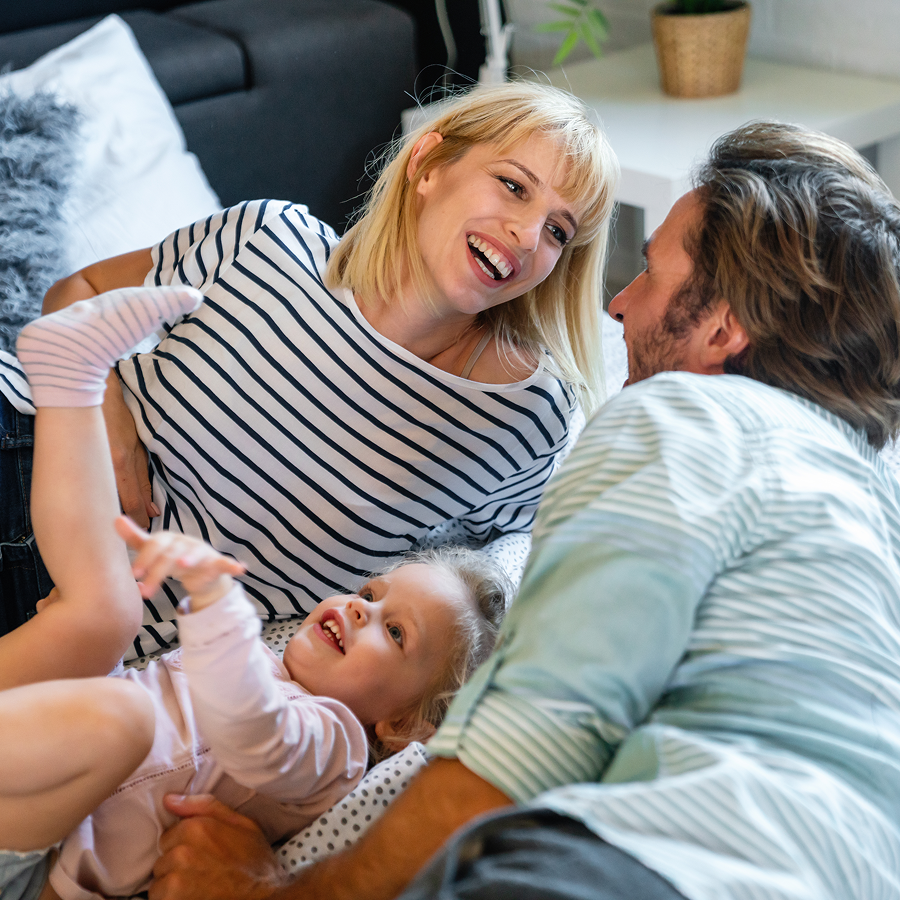 A man and woman are playing with a little girl on a couch.