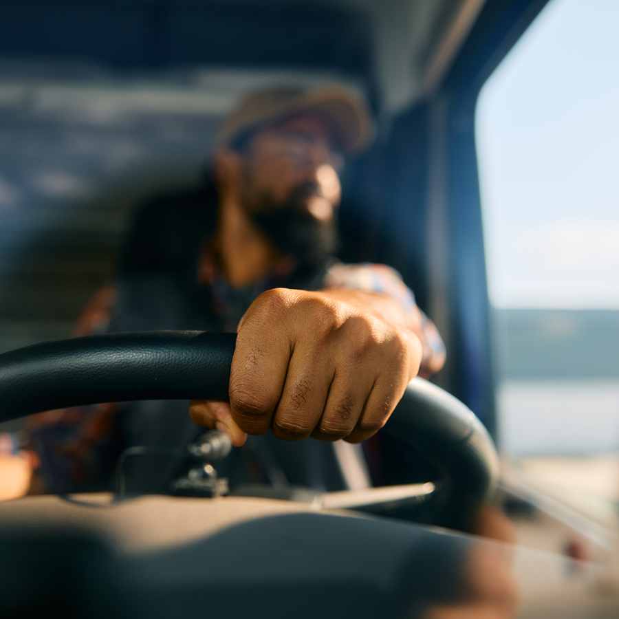 A man is driving a truck with his fist on the steering wheel.