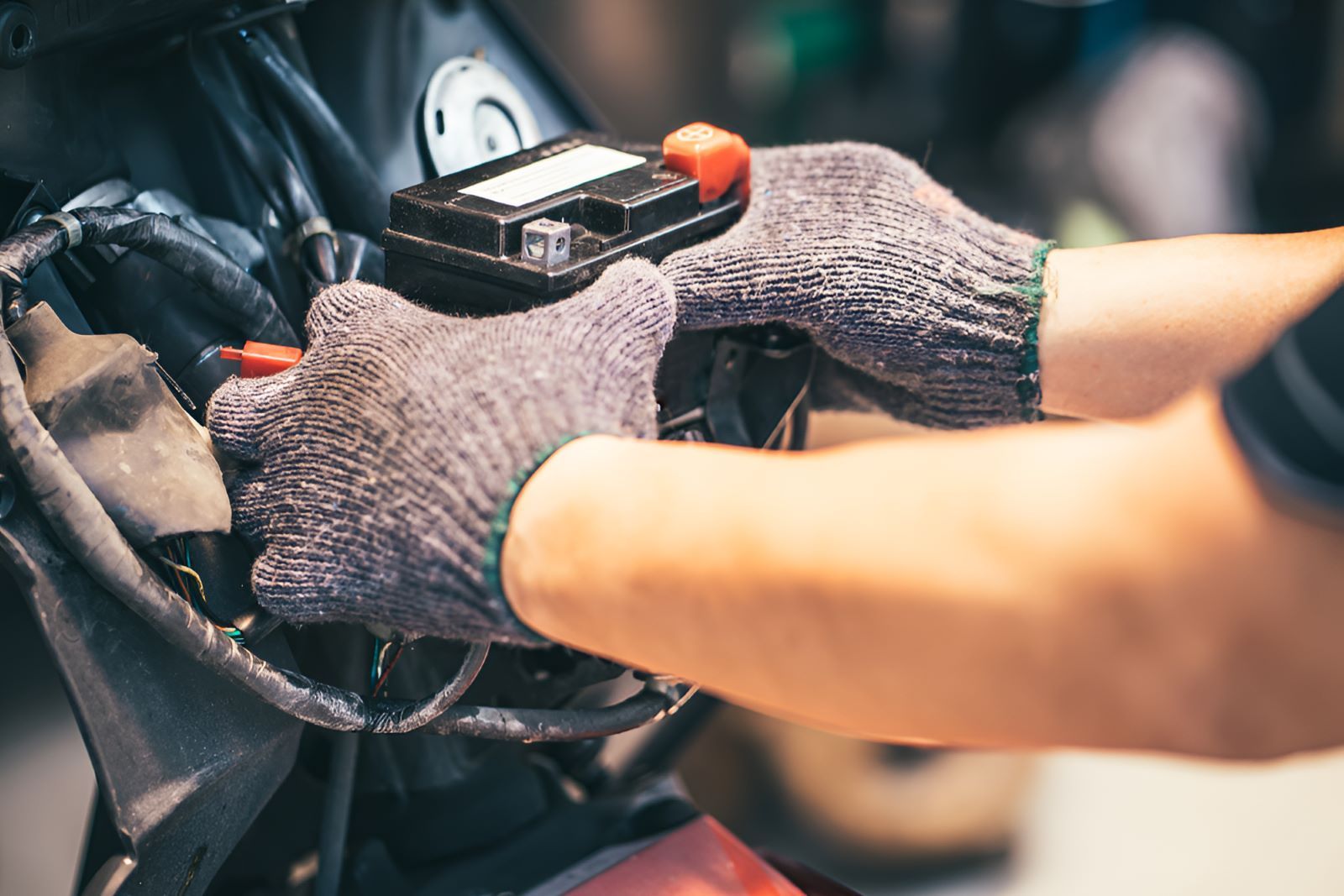 A Person Wearing Gloves Is Working On A Motorcycle Battery — All Models Service Centre In Port Macquarie, NSW