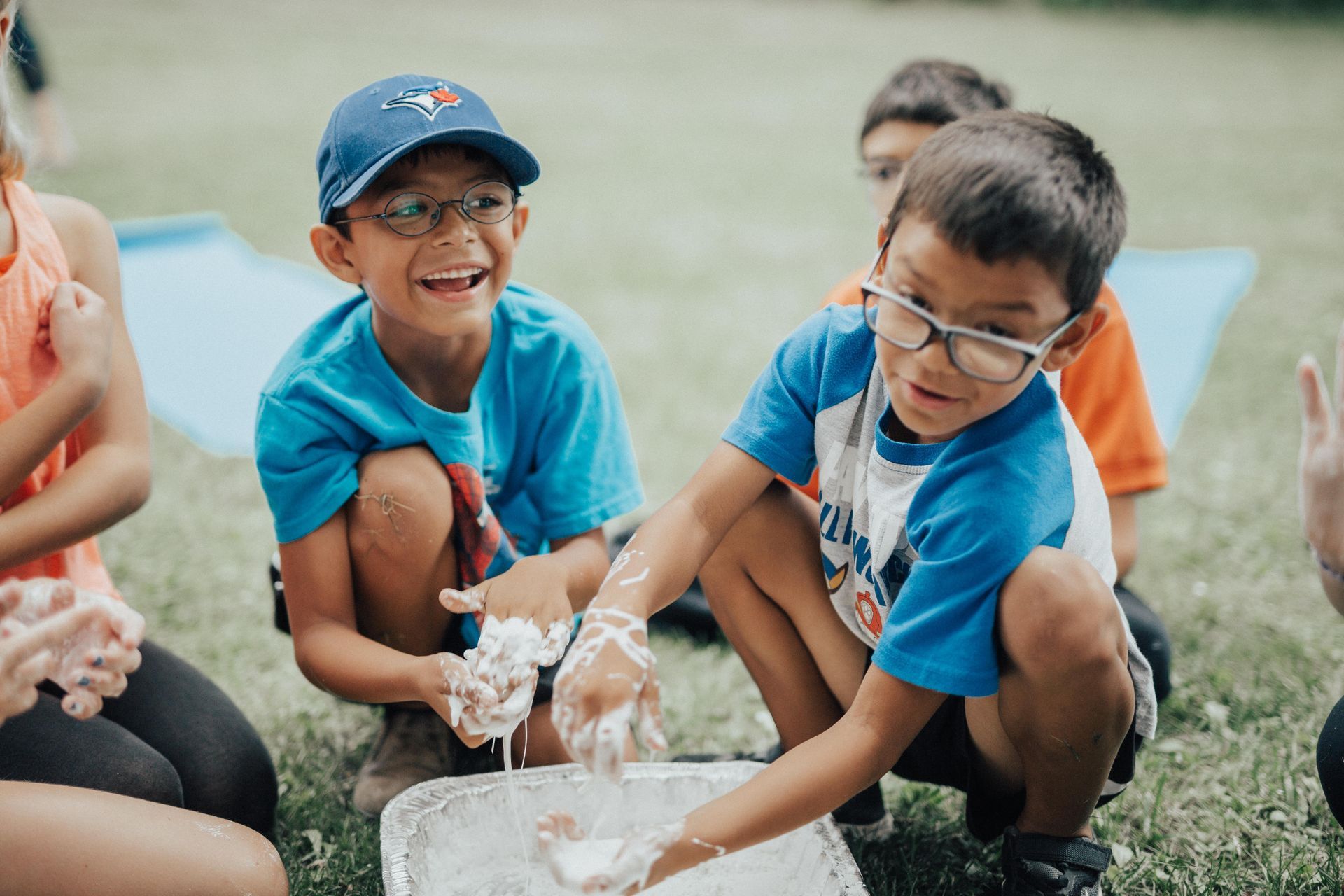 Children squatting on the grass with their hands in a goopy mess as they play and laugh together