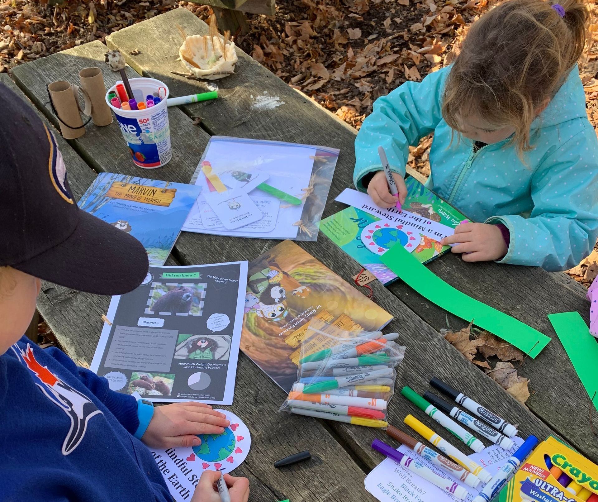 Kids sitting at a picnic table, colouring with Marvin the Marmot books