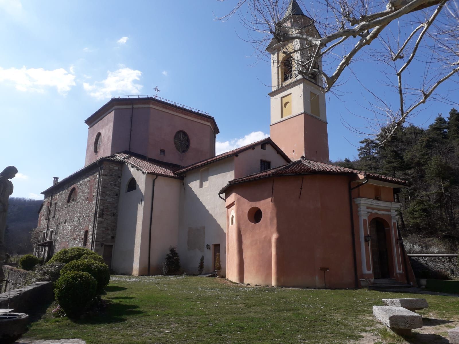 Chiesa con pareti in pietra e stucco rosa, alto campanile, cielo azzurro ed erba verde.