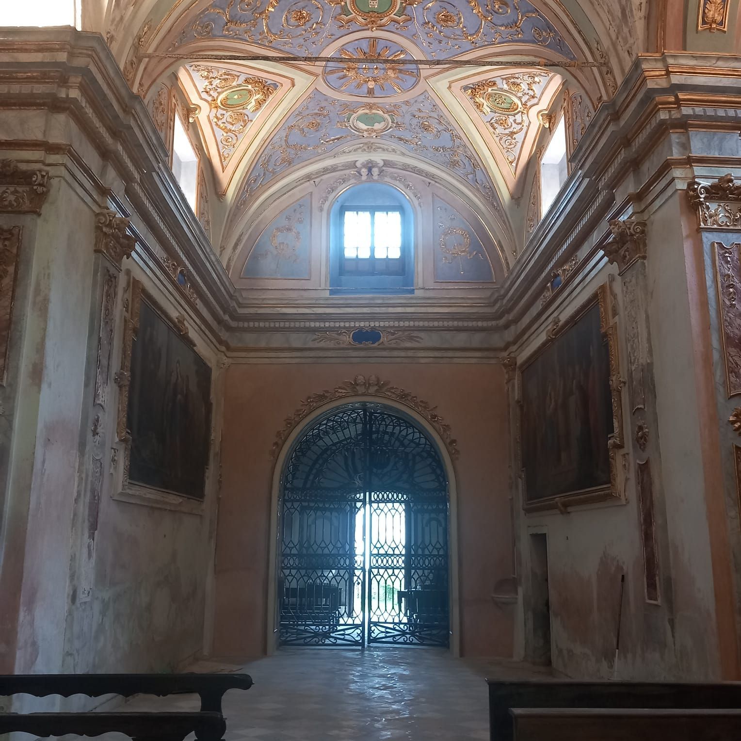 Interno di una chiesa riccamente decorata con soffitto a volta, dipinti e un cancello in ferro battuto