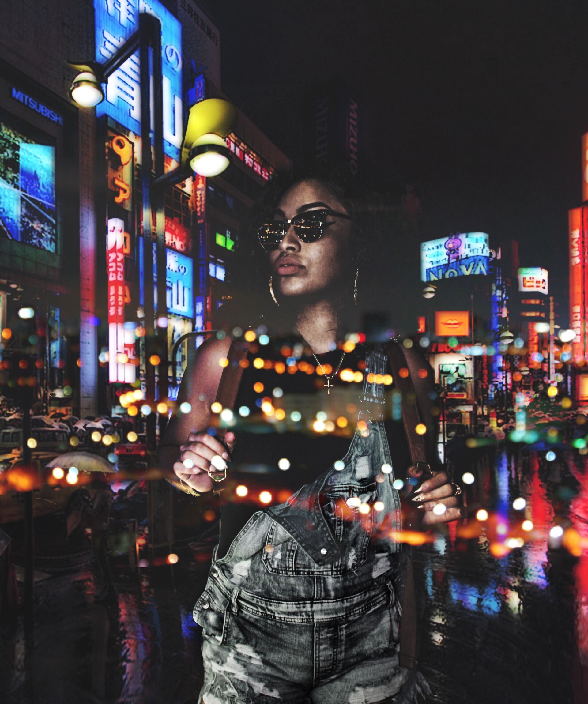 Woman in sunglasses standing in a neon-lit city street at night, with colorful reflections around her