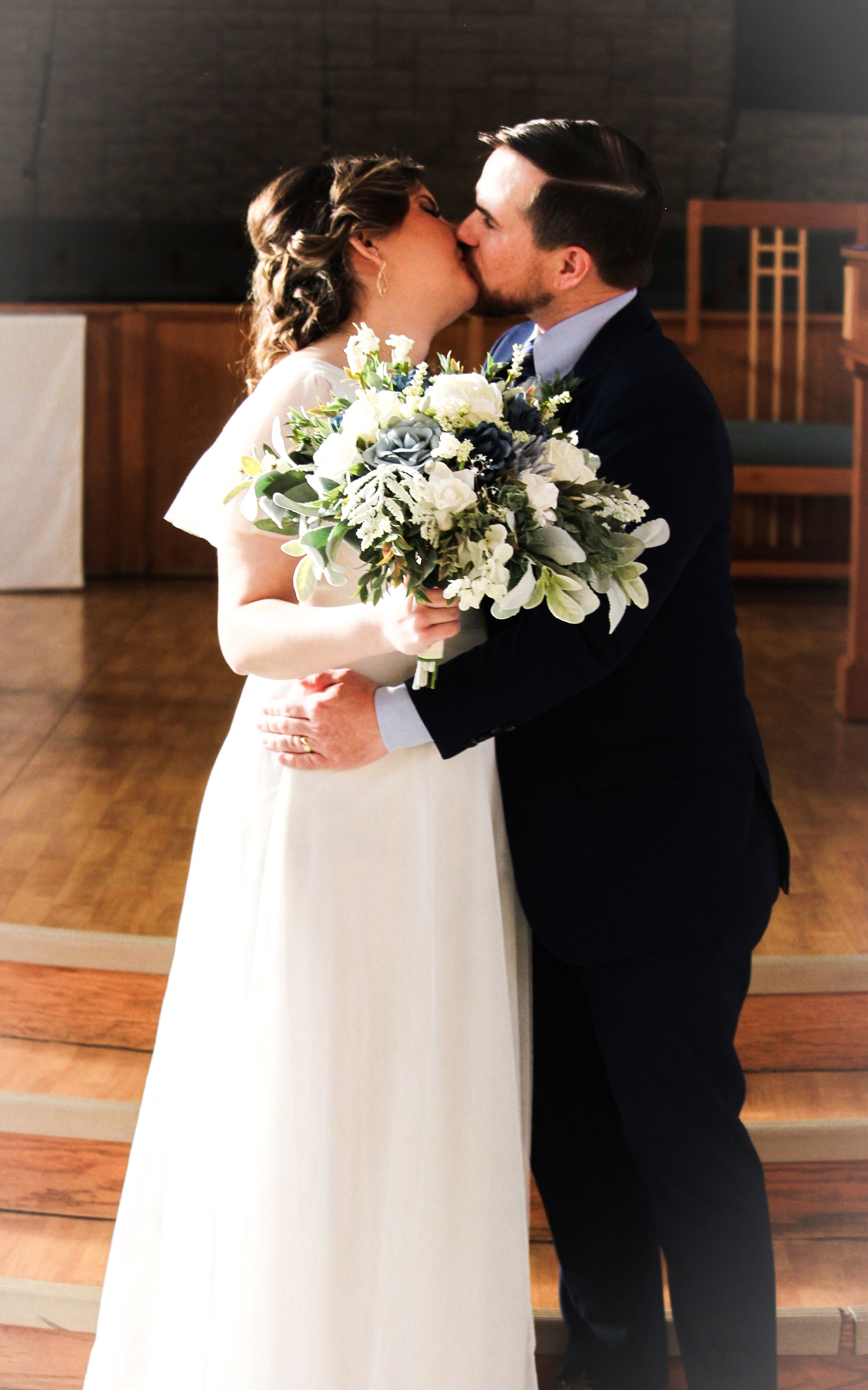 Bride and groom kissing indoors, bride holding a white bouquet in a sunlit hall