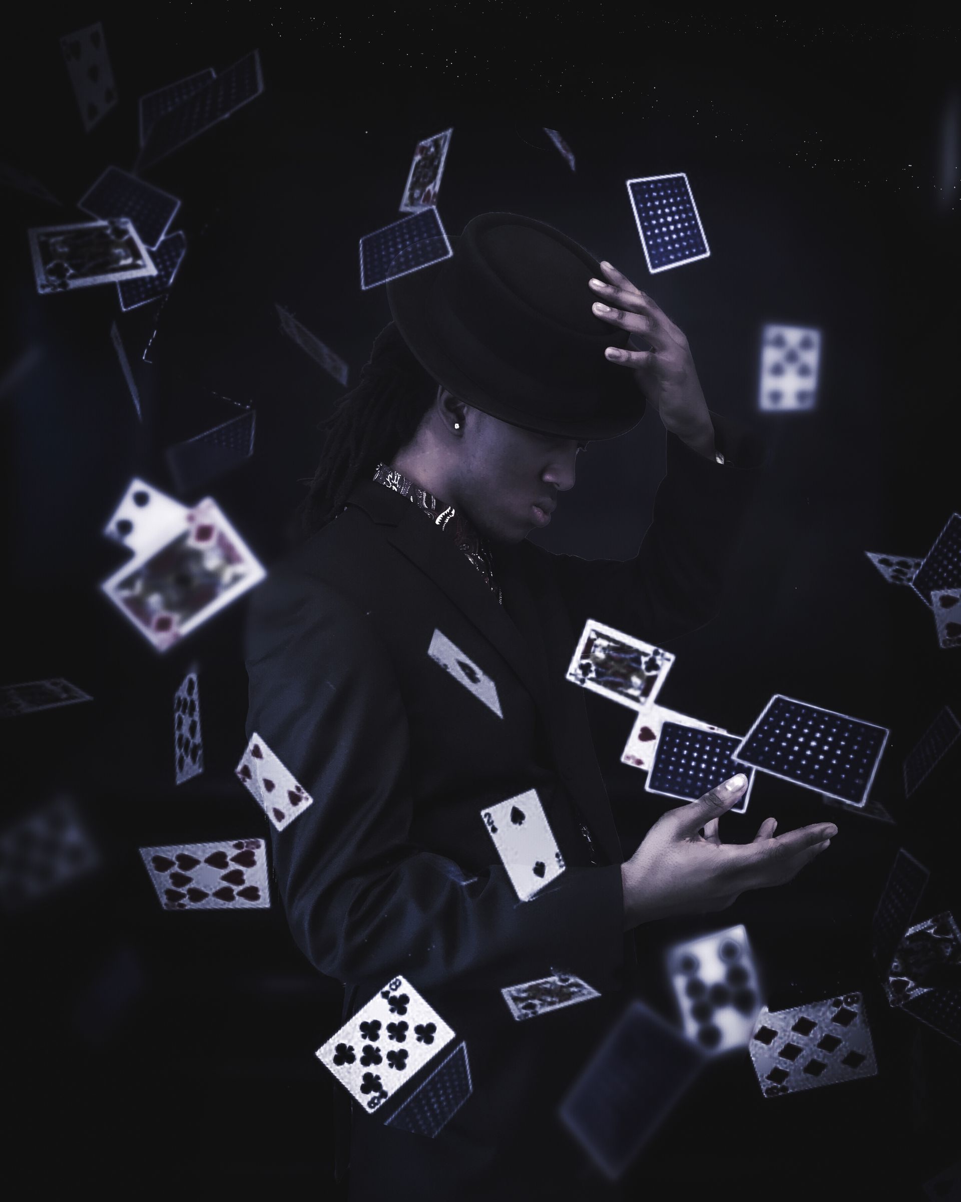 Person in dark clothing and hat, surrounded by floating playing cards in a moody, low-light scene